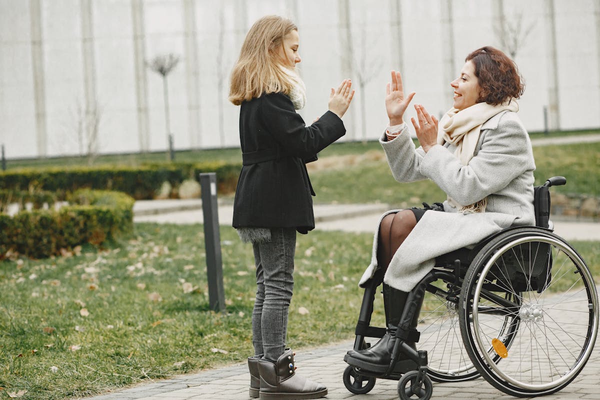 A mother in a wheelchair playing with her daughter outdoors